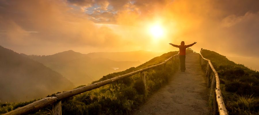 Woman on path at top of mountain with sun rising in background. Woman has her arms outstreatched represeting freedom.